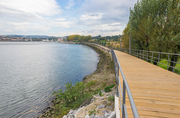 Fototapeta na wymiar River lake water pier wooden catwalk bank way path cycling track urban park city horizon background