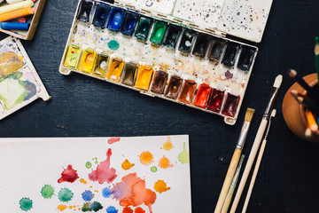 From above shot of workplace with palette of watercolors, paintbrushes and sketch book.