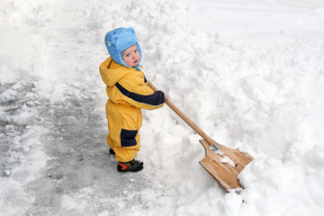 Little boy with big wooden shovel to clear snow. A very snowy wi