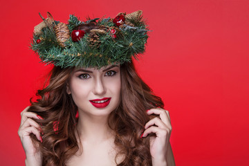 Christmas or New Year beauty girl portrait isolated on red background. Beautiful woman with luxury makeup and christmas wreath on head. Christmas mood.