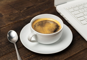 White cup of coffee with spoon and notebook on natural wooden table.