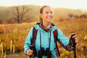 Happy young woman hiking with sticks and backpack during beautiful sunny autumn, fall