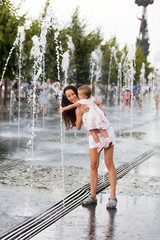 Naklejka premium Mother and child playing with water jets of the fountain on a hot summer day
