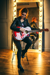 redhead rock girl in black leather jacket and black boots plays the red guitar