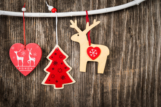 Red Christmas decorations hanging on branch over wooden background