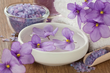 Obraz na płótnie Canvas SPA treatment set / Floating violet flower in water, aromatic essential oil, sea salt, soft towel and on wooden background