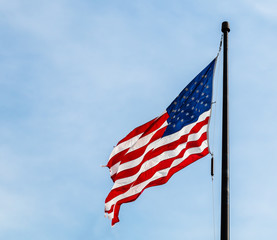 American flag flying on from a black flagpole against a cool blue sky.
