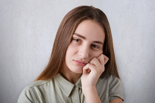 A pretty young girl with brown eyes with full lips and long straight brown hair having a sad look and keeping her hand on her cheek. A portrait of an attractive grieved girl on the white background