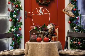 Fototapeta na wymiar Red door porch with Christmas wreath and holiday decorations on the table