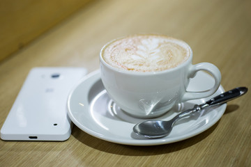 Coffee cappuccino in white cup and white mobile phone on the table in a cafe

