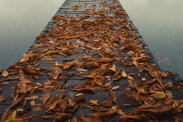 Papier Peint photo autocollant Jetée Wooden pier with leaves on the quiet lake in autumn