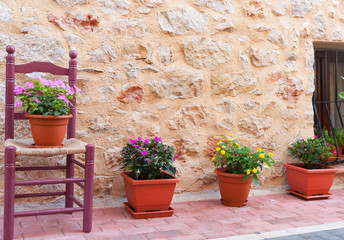 Fototapeta na wymiar Chair and flower pots decorate home exterior in narrow Spanish street.