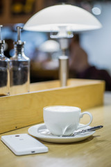 Coffee cappuccino in white cup and white mobile phone on the table in a cafe

