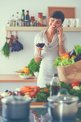 Young woman cutting vegetables in kitchen, holding a glass of wine