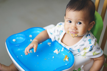 Asian baby eating food by himself