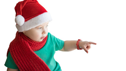 Little boy in Christmas hat and red scarf shows something with his finger. Isolated on white background.
