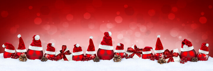 row of red christmas baubles balls in snow with santa claus hats on red bokeh background