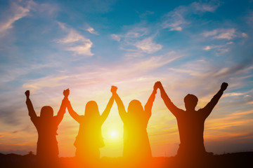 Silhouette of happy business team making high hands in sunset sky