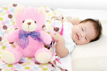 Portrait of adorable baby girl sleeping on the bed with bear dol