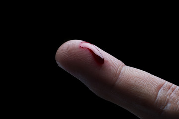 Drop of blood on finger on black background