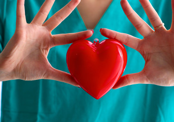 Young woman doctor holding a red heart, in office