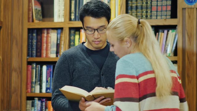 Friends talking in the college library. Asian man and Caucasian woman attractive