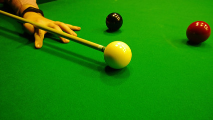 Male hand with a pool cue preparing to hit the white ball on the game of snooker