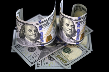 Two half rolled hundred us dollar banknotes standing on octagon made of hundred usa dollars bills. Isolated on black background.