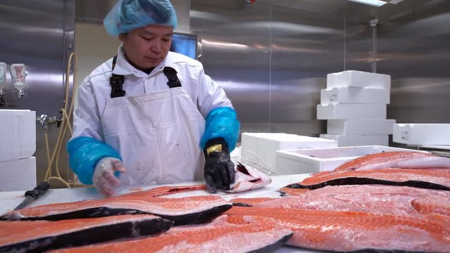 Asian man slicing a fillet of salmon at table in a fish shop. Dolly shot.