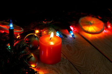 New year copyspace card. Christmas tree fir branch, burning candle, colorful lights garland,  dry oranges on wooden background.