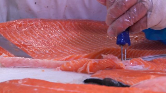 Man slicing a fillet of salmon at table in a fish shop.