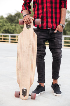 Cropped photo of young dark skinned guy holding his skateboard