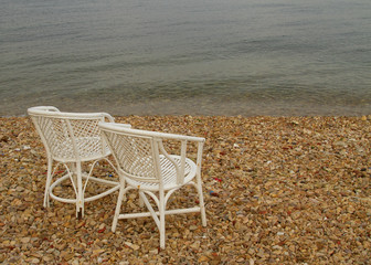 Two white empty chairs on the pebble beach