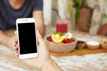 Young female using smart phone while having lunch at cafe. Caucasian woman holding electronic device with blank screen with copy space for your promotional content. Selective focus on mobile
