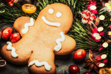 Smiling gingerbread men with fir branches, spices and  festive bokeh lighting, close up