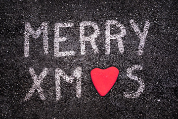 Merry xmas written on asphalt road, red stone in the shape of a heart