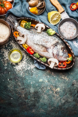 Fish and vegetables cooking with ingredients, dorado in baking form , preparation on rustic kitchen table with knife , oil and spices, top view, border. Healthy food or diet food concept.