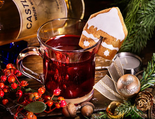 Close up of glass mug of mulled punch decorated ginger snap and Christmas ball. Gingerbread cookie in form of house on mug.