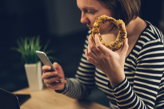 Woman Eating Sesame Bagel And Using Mobile Phone