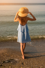 Woman standing on the beach. Young lady in wicker hat. Step towards the sea. Waiting for a miracle.