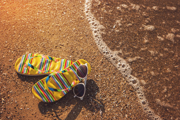 Flip flops with sunglasses. Footwear on a shore. Go to the sea. Spend holidays at tropical island.