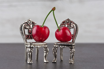 A couple of red ripe cherries on miniature silver chairs. Relationship concept