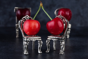 Red delicious ripe cherries on vintage silver chairs and dark background