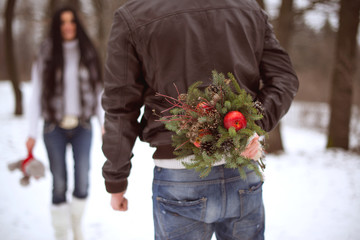 Young man holding winter bouquet behind his back dating girlfriend and celebrating valentines day. Couple in love outdoor. Christmas portrait in park