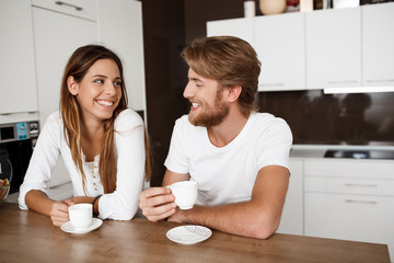 Young beautiful couple sitting at kitchen drinking morning coffee smiling.