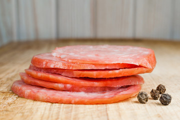 Thinly sliced pieces of salami on a cutting board. Wooden background.