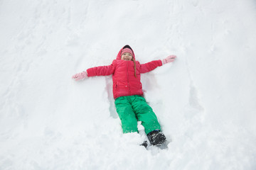 Fototapeta na wymiar Playful girl playing in snow, making a snow angel