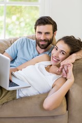 Portrait of young couple lying on sofa and using laptop