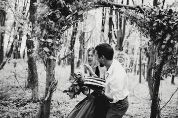 Happy beautiful couple near the wedding arch holding a cake b&w