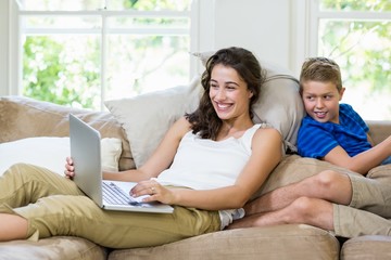 Obraz premium Mother and son sitting on sofa and using laptop